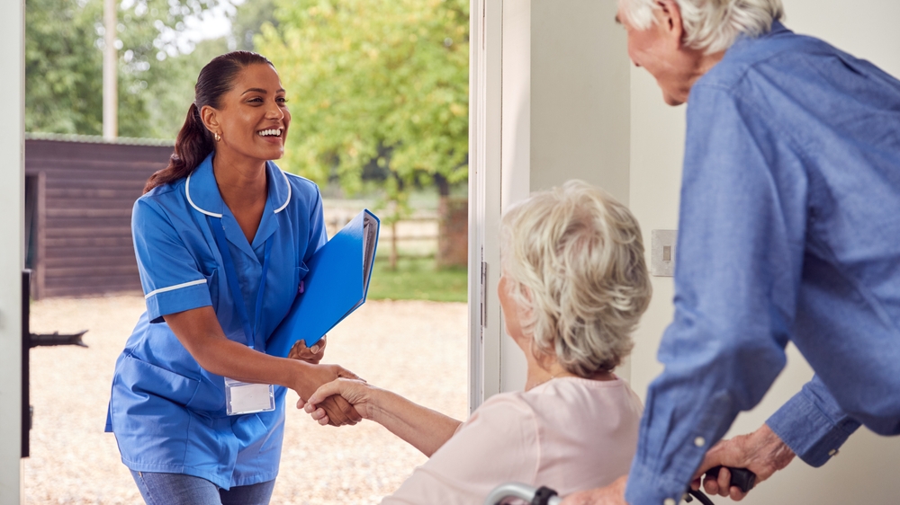 Senior,Couple,With,Woman,In,Wheelchair,Greeting,Nurse,Or,Care