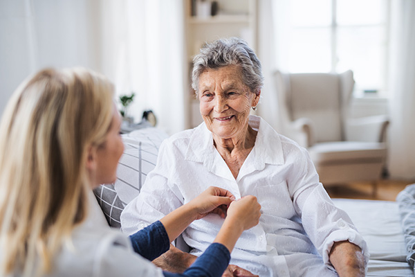 A health visitor helping a sick senior woman sitting on bed at home.